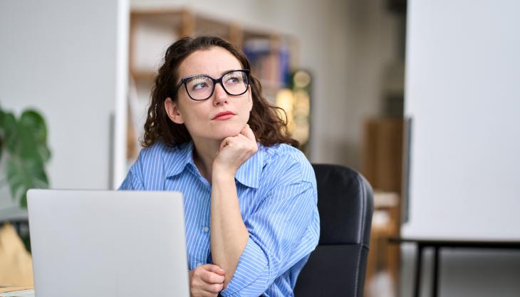 Eine Frau sitzt nachdenklich an einem Laptop und schaut in die Ferne.