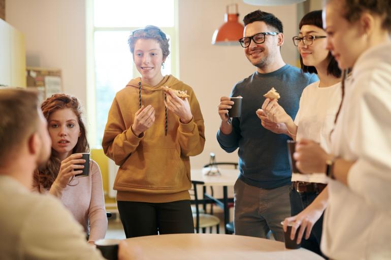 Gruppe Menschen steht in Kaffeeküche zusammen und unterhält sich.