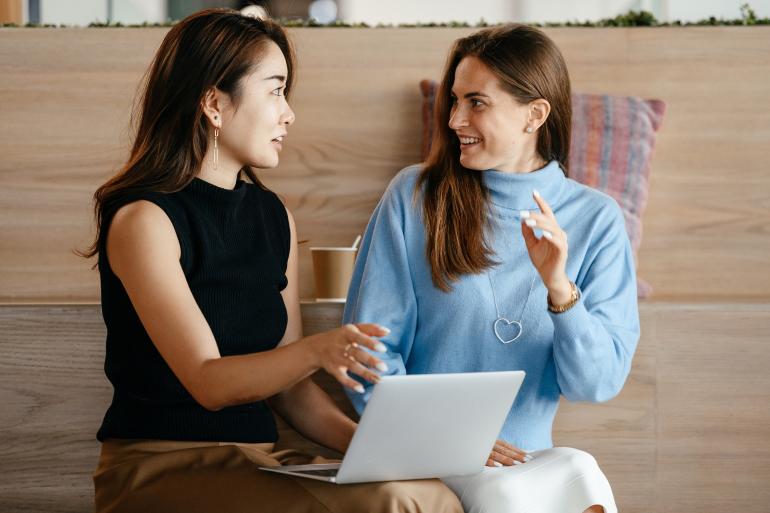 Zwei Frauen diskutieren mit einem Laptop auf dem Schoß.