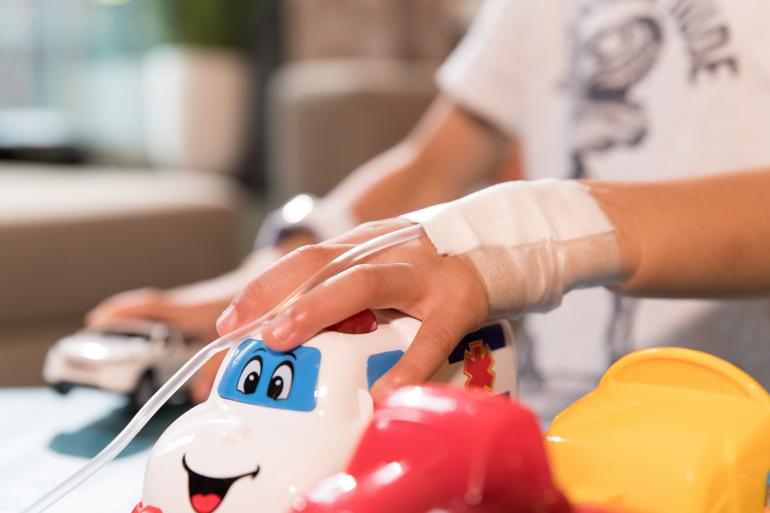 Ein Kind mit einer Drainage am Handgelenk greift nach einem Spielzeugauto.