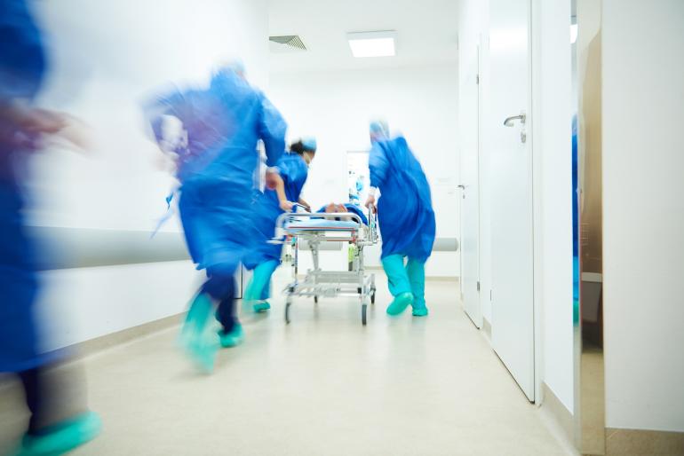 Krankenhauspersonal schiebt eilig einen Patienten oder eine Patientin auf der Liege über den Flur.