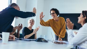 Zwei Mitarbeitende geben sich High Five, während die umsitzenden Teammitglieder klatschen