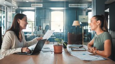 Zwei Businessfrauen sitzen sich an einem Arbeitstisch im Office gegenüber