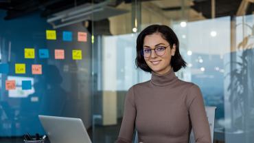 Eine junge Frau sitzt am Laptop, im Hintergrund hängen Post-its an einer Glaswand.