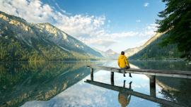 Eine Person sitzt auf dem Steg eines glasklaren Bergsees.