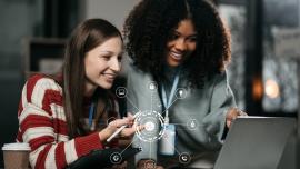 Zwei junge Frauen schauen auf einen Laptop. Symbole für KI, digitale Technik.