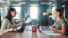 Zwei Businessfrauen sitzen sich an einem Arbeitstisch im Office gegenüber