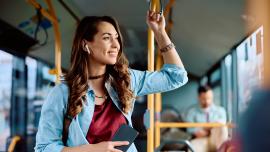 Eine junge Frau steht im Bus und hört über Bluetooth-Ohrstöpsel einen Podcast.