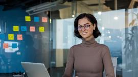 Eine junge Frau sitzt am Laptop, im Hintergrund hängen Post-its an einer Glaswand.