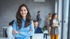 Eine junge Frau in Businesskleidung steht vor einem Bürohintergrund.