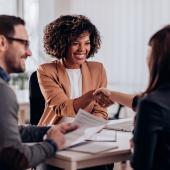 Einer Frau wird von zwei Recruitern zum erfolgreichen Bewerbungsgespräch gratuliert.