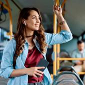 Eine junge Frau steht im Bus und hört über Bluetooth-Ohrstöpsel einen Podcast.
