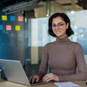 Eine junge Frau sitzt am Laptop, im Hintergrund hängen Post-its an einer Glaswand.
