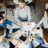 5 Mitarbeitende sitzen an einem runden Tisch mit Arbeitsmaterialien