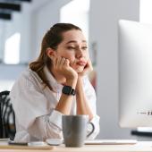 Foto: Drobot Dean - Adobe Stock Eine junge Frau sitzt gelangweilt vor einem weißen PC-Bildschirm, im Hintergrund sitzt eine andere Mitarbeiterin.