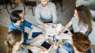 5 Mitarbeitende sitzen an einem runden Tisch mit Arbeitsmaterialien