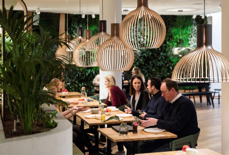 Mitarbeiterbereich bei HRS: Menschen sitzen an kleinen Tischen und essen.
