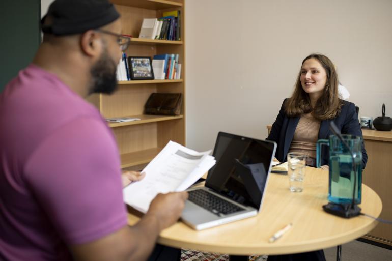 Schauspieler und Studierende sitzen sich in der Gesprächssimulation an einem Konferenztisch gegenüber und reden miteinander.