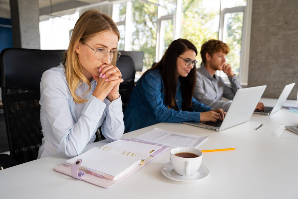Eine Frau sitzt still und nachdenklich vor ihren Unterlagen. Neben ihr am Tisch sitzen zwei Kolleg*innen.