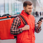 Ein Lieferant mit Rucksack schaut auf sein Handy.