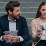 Ein Mann mit vielen Geldscheinen und eine Frau mit wenigen Geldscheinen sitzen nebeneinander.