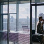 Ein Mann trinkt alleine in einem schicken Büro mit Ausblick über die Stadt einen Kaffee.
