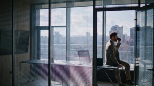 Ein Mann trinkt alleine in einem schicken Büro mit Ausblick über die Stadt einen Kaffee.