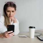 Eine Frau sitzt am Arbeitstisch und schaut auf ihr Smartphone