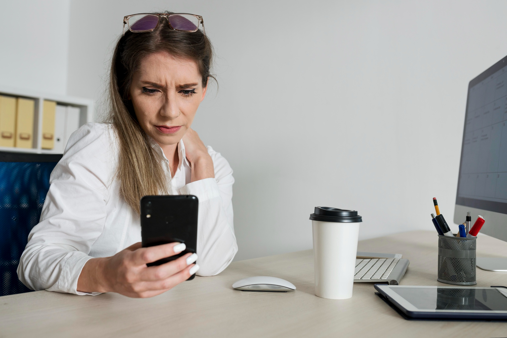 Eine Frau sitzt am Arbeitstisch und schaut auf ihr Smartphone