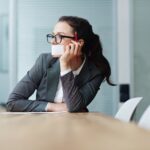 Eine Frau mit einem Blatt Papier vor dem Mund stützt frustriert den Kopf in die Hand.
