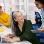3 Personen in einem Büro, eine junge Frau stellt einer Kollegin eine Frage.