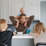 Eine Frau hat ein Kleinkind auf den Schultern, vor ihr sitzen zwei weitere Kinder.