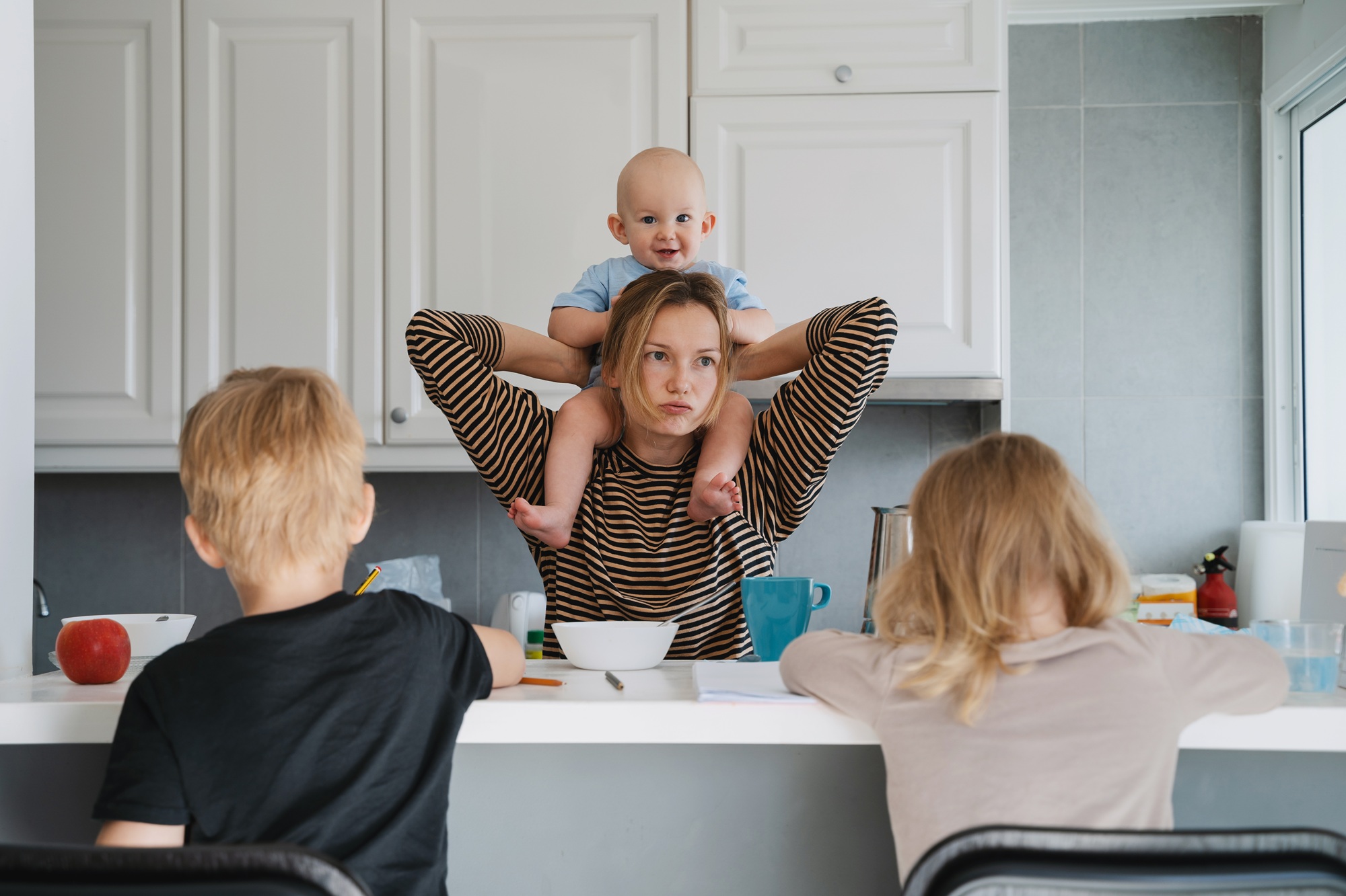 Eine Frau hat ein Kleinkind auf den Schultern, vor ihr sitzen zwei weitere Kinder.
